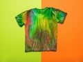 A stylish hand-painted tie dye T-shirt on an orange and green background. Flat lay