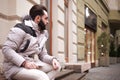 Stylish handsome man with a beard in a winter jacket with fur posing outdoors. Portrait of an elegant guy in beautiful clothes Royalty Free Stock Photo