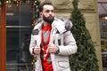 Stylish handsome man with a beard in a winter jacket with fur posing outdoors. Portrait of an elegant guy in beautiful clothes Royalty Free Stock Photo