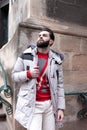 Stylish handsome man with a beard in a winter jacket with fur posing outdoors. Portrait of an elegant guy in beautiful clothes Royalty Free Stock Photo