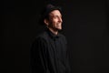 Stylish handsome man a black shirt and pork pie hat smiling isolated over black background. Royalty Free Stock Photo