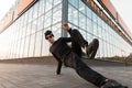 Stylish handsome young hipster man in fashionable dark sunglasses in trendy black clothes dancing break dance