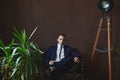 A stylish handsome young man in a fashionable blue suit sits on the sofa at dark interior