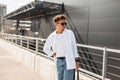 Stylish handsome young man hipster in sunglasses in fashionable clothes with trendy hairstyle with bag posing Royalty Free Stock Photo