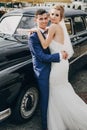 Stylish happy bride and groom embracing at old black retro car. Gorgeous wedding couple of newlyweds hugging after wedding Royalty Free Stock Photo