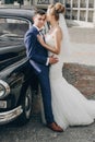 Stylish happy bride and groom kissing at old black retro car. Gorgeous wedding couple of newlyweds embracing after wedding Royalty Free Stock Photo