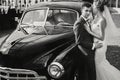 Stylish happy bride and groom kissing at old black retro car. Gorgeous wedding couple of newlyweds embracing after wedding Royalty Free Stock Photo