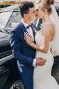 Stylish happy bride and groom kissing at old retro car. Gorgeous wedding couple of newlyweds embracing after wedding ceremony. Royalty Free Stock Photo