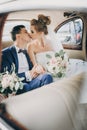 Stylish happy bride and groom showing hands with wedding rings, sitting inside of old retro car. Gorgeous wedding couple of Royalty Free Stock Photo