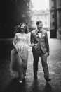 Stylish happy bride and groom walking on background of old church in rainy street. Provence wedding. Beautiful emotional wedding Royalty Free Stock Photo