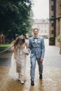 Stylish happy bride and groom walking on background of old church in rainy street. Provence wedding. Beautiful emotional wedding Royalty Free Stock Photo