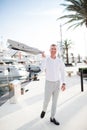 Stylish happy businessman is wearing white fashion costume stands on the background of the bay with luxury yachts Royalty Free Stock Photo