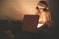 Stylish happy girl in santa hat and cozy sweater opening christmas gift box with magic light in dark room. Young hipster woman Royalty Free Stock Photo