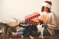 Stylish happy girl in santa hat and her cats opening christmas gift box with magic light in decorated christmas room. Young Royalty Free Stock Photo