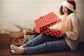 Stylish happy girl in santa hat opening christmas gift box with magic light. Young hipster woman in cozy sweater opening magical Royalty Free Stock Photo