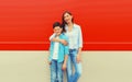 Stylish happy smiling mother with son teenager posing together in checkered shirts, jeans in the city on vivid red background Royalty Free Stock Photo