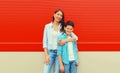 Stylish happy smiling mother with son teenager posing together in checkered shirts, jeans in the city on vivid red background Royalty Free Stock Photo