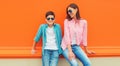 Stylish happy smiling mother with son teenager posing together in sunglasses, checkered shirts, jeans in the city on vivid orange Royalty Free Stock Photo