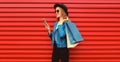 Stylish happy smiling woman with shopping bags and smartphone wearing blue jacket, black round hat on red background Royalty Free Stock Photo