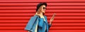 Stylish happy smiling woman with shopping bags and smartphone wearing blue jacket, black round hat on red background Royalty Free Stock Photo