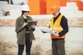 Stylish happy woman architect with tablet and senior foreman checking blueprints at construction site. Engineer and construction Royalty Free Stock Photo