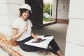 Stylish happy woman engineer in hard hat looking at digital plans on tablet while sitting in window of new modern house. Young Royalty Free Stock Photo