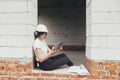 Stylish happy woman engineer in hard hat looking at digital plans on tablet while sitting in window of new modern house. Young Royalty Free Stock Photo