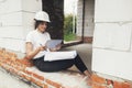 Stylish happy woman engineer in hard hat looking at digital plans on tablet while sitting in window of new modern house. Young Royalty Free Stock Photo