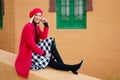 Stylish happy woman sitting on border near aged colored building