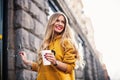 Stylish happy young woman wearing boyfrend jeans, white sneakers bright yellow sweetshot.She holds coffee to go. portrait of smili Royalty Free Stock Photo