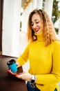 Happy young woman is wearing a pink scarf, She is holding a coffee to go. Portrait of smiling girl in autumn city. Royalty Free Stock Photo