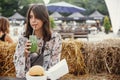Stylish hipster boho girl drinking smoothie in glass jar with delicious vegan burger on wooden table at street food festival.