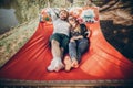 Stylish hipster couple cuddling and relaxing in hammock in sunny summer park. man hugging woman and resting in forest, smiling