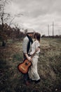 Stylish hipster couple hug in field, handsome cowboy musician wi