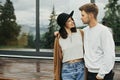 Stylish hipster couple hugging on wooden porch, relaxing in modern cabin in mountains. Happy young family in modern outfits