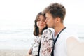 Stylish hipster couple taking selfie on beach and kissing at evening sea. Summer vacation. Portrait of happy young family on Royalty Free Stock Photo
