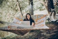 Stylish hipster freelancer with laptop relaxing in hammock in sunny summer park. girl looking at laptop, working and smiling.