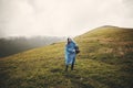 Stylish hipster girl in blue raincoat and with backpack standing on top of misty mountains and clouds. Funny young woman traveler Royalty Free Stock Photo