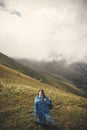 Stylish hipster girl in blue raincoat and with backpack standing on top of misty mountains and clouds. Young woman traveler Royalty Free Stock Photo