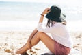 Stylish hipster girl in hat sitting on beach and tanning near sea waves. Summer vacation. Happy boho woman relaxing and enjoying Royalty Free Stock Photo
