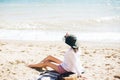 Stylish hipster girl in hat sitting on beach and tanning near sea waves. Summer vacation. Happy boho woman relaxing and enjoying Royalty Free Stock Photo