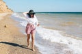 Stylish hipster girl in hat walking on beach and smiling. Summer vacation. Happy young boho woman relaxing and enjoying sunny warm Royalty Free Stock Photo