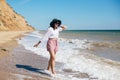 Stylish hipster girl in hat walking on beach and smiling. Summer vacation. Happy young boho woman relaxing and enjoying sunny warm Royalty Free Stock Photo