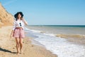 Stylish hipster girl in hat walking on beach and smiling. Summer vacation. Happy young boho woman relaxing and enjoying sunny warm Royalty Free Stock Photo