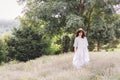 Stylish hipster girl in linen dress and hat relaxing in lavender field near tree. Happy bohemian woman enjoying summer vacation in Royalty Free Stock Photo