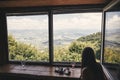 Stylish hipster girl looking on top of mountains through big window in old cabin. Young woman relaxing in summer mountains. Royalty Free Stock Photo