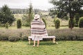 Stylish hipster girl in poncho, linen dress and hat posing at lavender field and relaxing in the morning. Bohemian woman enjoying