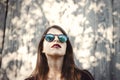 Stylish hipster girl posing in sunny street on background of wooden wall. Portrait of boho girl in cool outfit and sunglasses Royalty Free Stock Photo