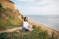 Stylish hipster girl sitting on beach and doing yoga. Happy boho woman practicing yoga and meditation at sea on tropical island.