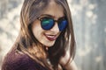 Stylish hipster girl smiling in sunny street on background of wooden wall. Boho girl in cool outfit and sunglasses posing in Royalty Free Stock Photo